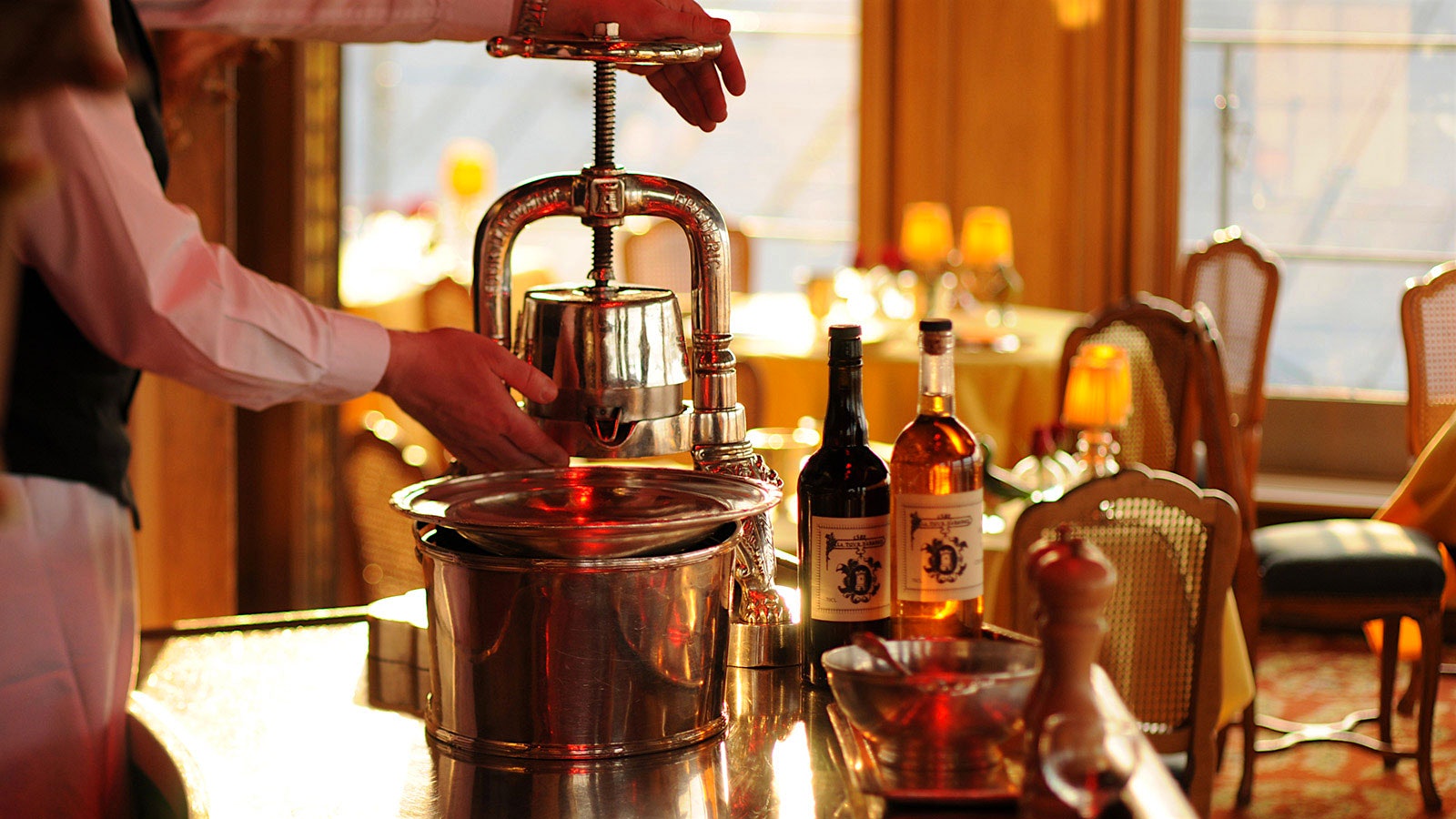 A waiter uses the duck press at La Tour d’Argent in Paris, next to bottles of wine.